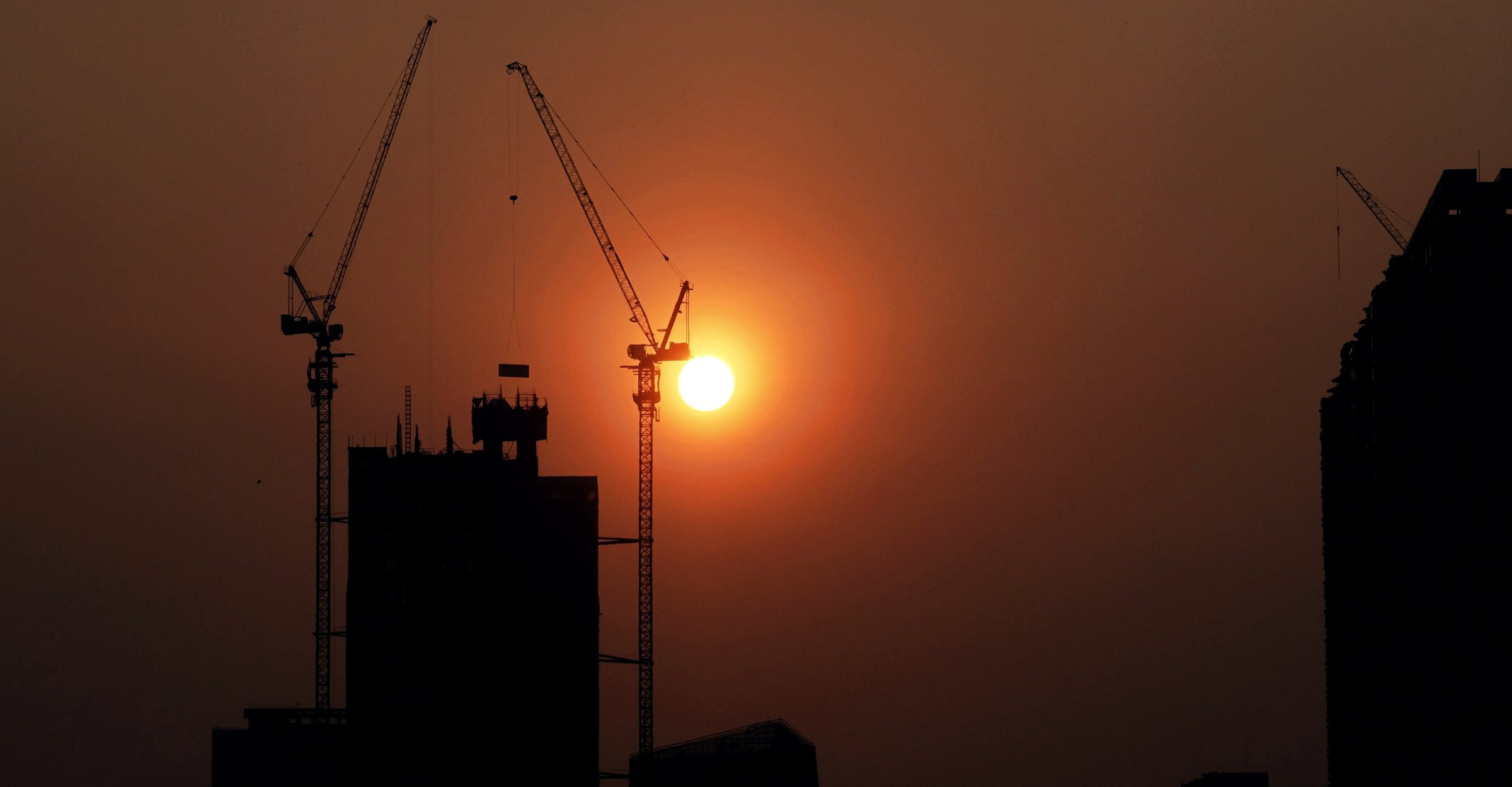 Construction cranes silhouetted against the setting sun