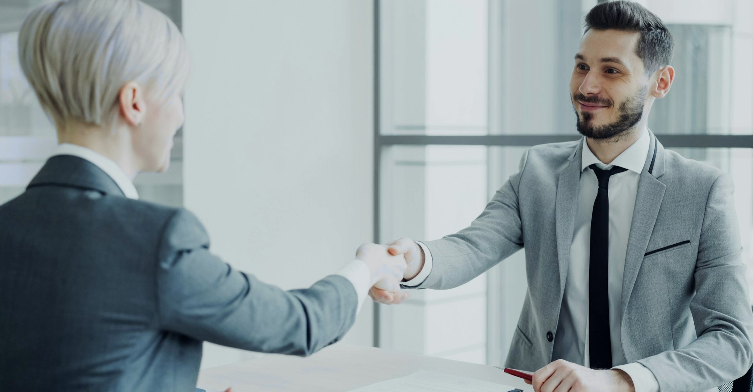 Two colleagues shaking hands across a desk